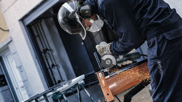 A person wearing safety equipment grinds metal, creating sparks.