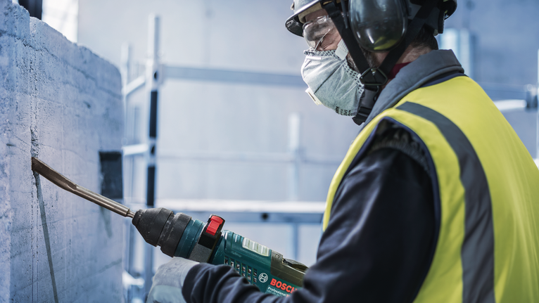Person wearing safety equipment chiseling concrete with a power tool.
