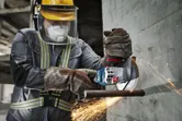 A person wearing safety equipment uses a cordless angle grinder to cut through rebar.