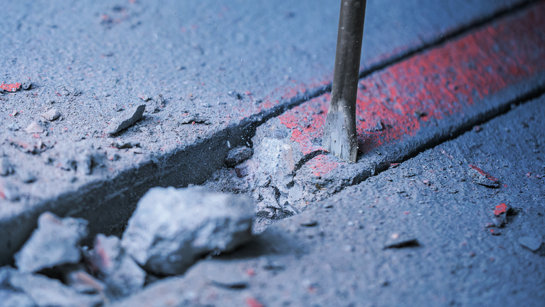 Chisel breaking concrete along a marked groove.