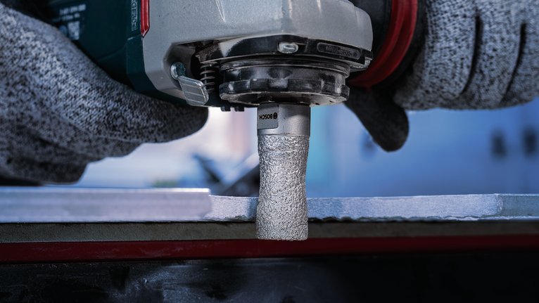 Person wearing safety equipment grinds a metal edge with a rotary tool.
