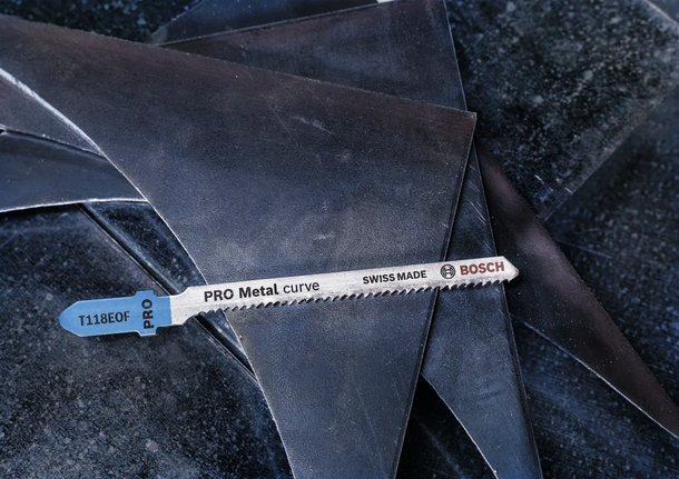 A metal jigsaw blade rests on stacked sheet metal pieces.