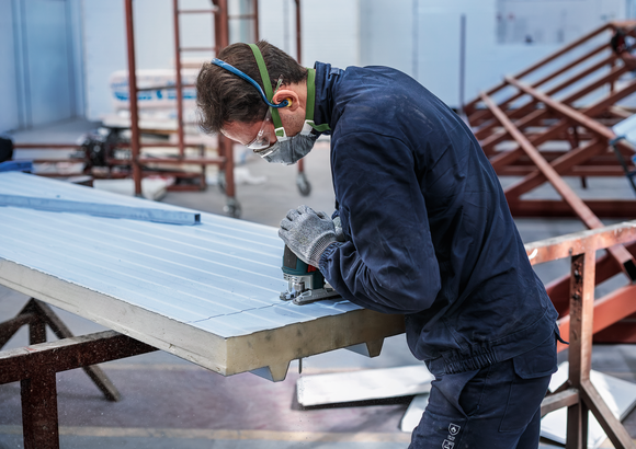 Person wearing safety equipment uses a jigsaw to cut grooves in an insulated panel.