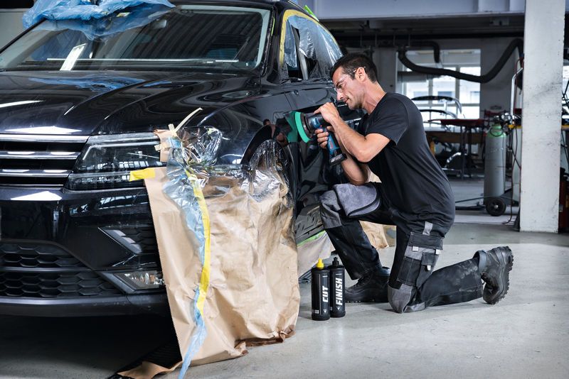 A person wearing safety equipment polishes a car door with a cordless polisher.