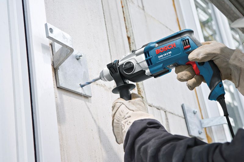 Electric impact drill with side handle attached, featuring a blue and silver casing.
