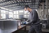 Person wearing safety equipment uses a straight grinder to grind a metal box.