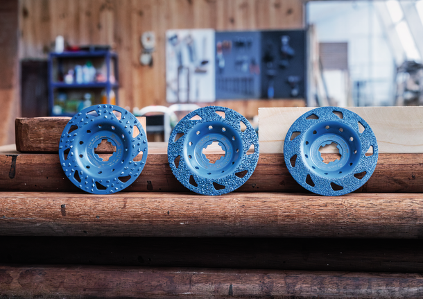 Three blue grinding wheels are displayed on stacked wooden beams in a workshop.