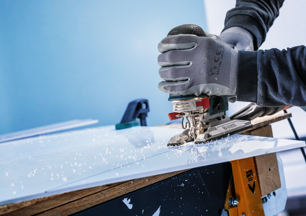 Worker wearing safety equipment cuts a plastic sheet with a jigsaw.