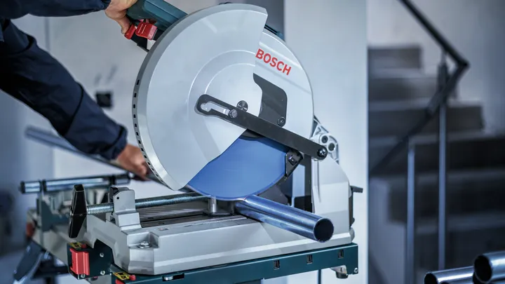 Person wearing safety equipment cuts a metal pipe with a circular saw.