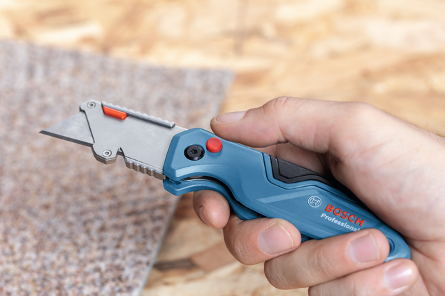 Person holding a blue utility knife, preparing to cut a piece of carpet.