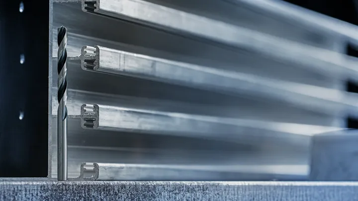 Metal drill bit positioned in front of stacked aluminum profiles.