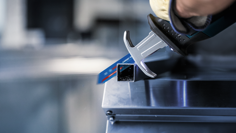 Person wearing safety equipment cuts a metal square tube with a reciprocating saw.