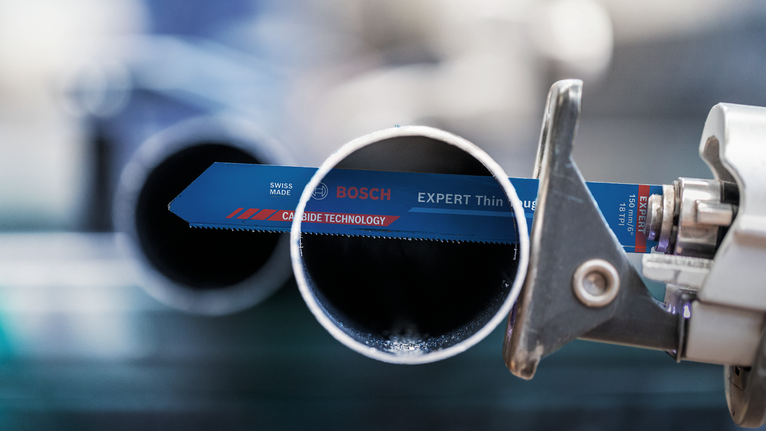 Reciprocating saw blade cutting through a metal pipe in an industrial setting.