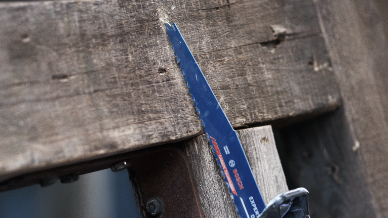 Reciprocating saw blade cutting through a thick wooden board.