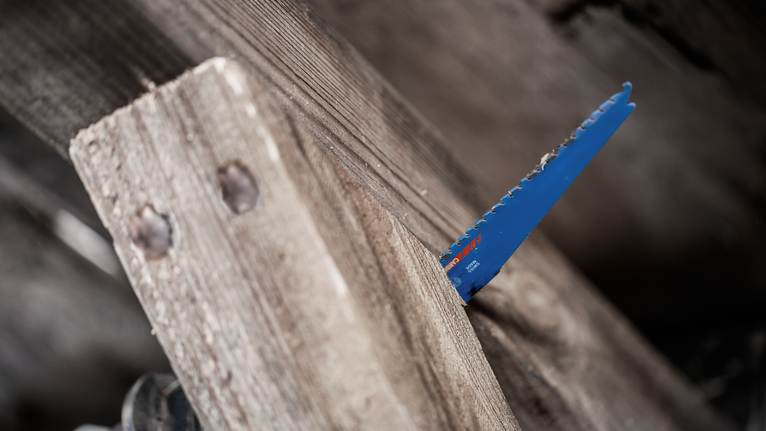 A reciprocating saw blade cutting through a rough wooden plank.