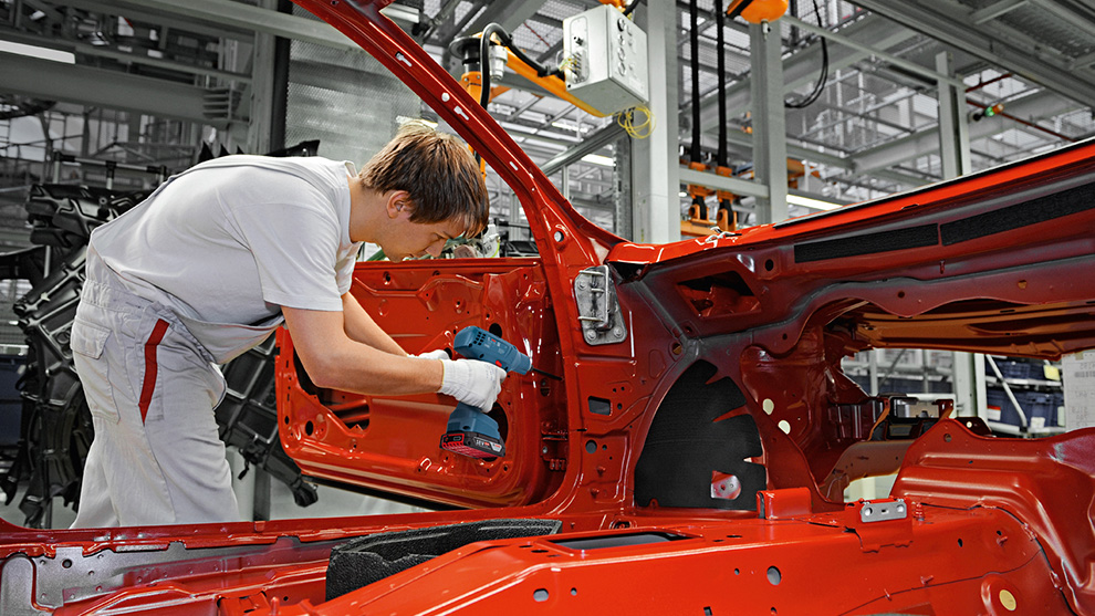 En man i arbetskläder använder en blå Bosch Professional skruvdragare i en röd bil.