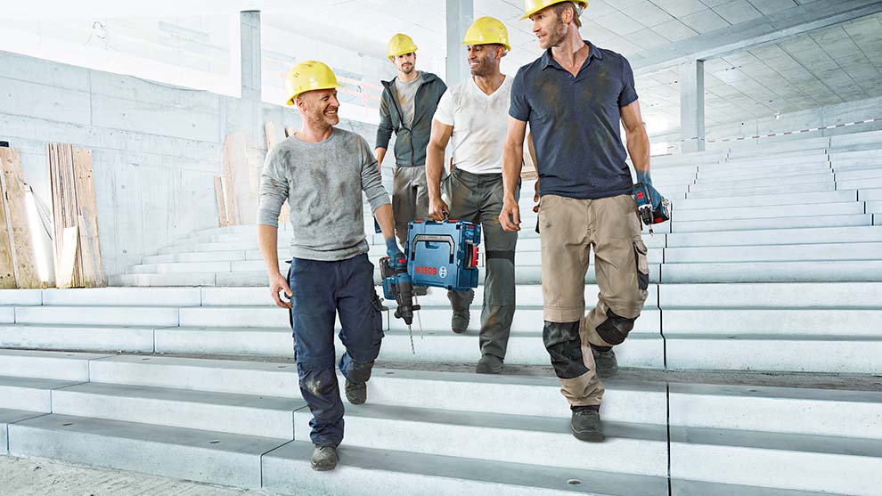 Fyra hantverkare med gula hjälmar går nerför en trappa med verktyg i händerna.