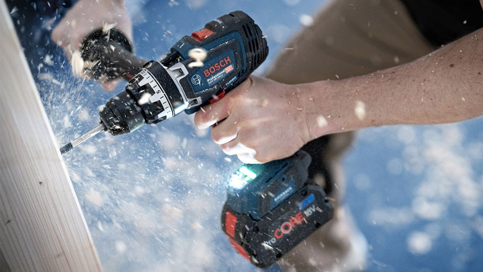 En Bosch Professional borrmaskin används på trä, spån flyger runt.