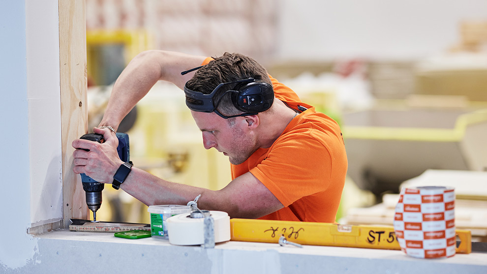 En man i orange tröja borrar med en Bosch Professional borrmaskin i en vägg.