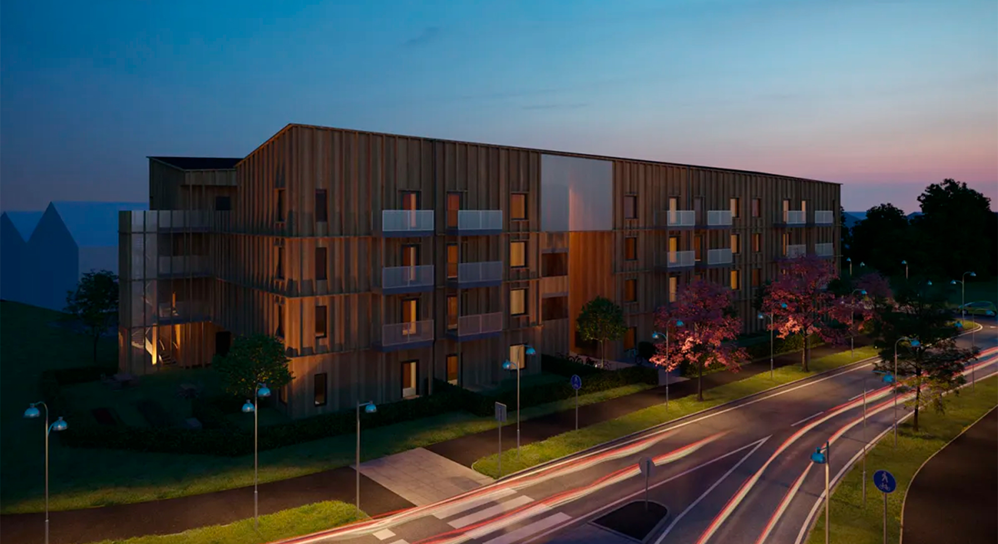 En modern träbyggnad vid väg med belysning och blommor i skymning.