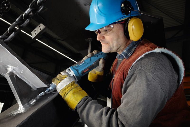 En person som bär säkerhetsutrustning slipar en metallkonstruktion med en rak slipmaskin.