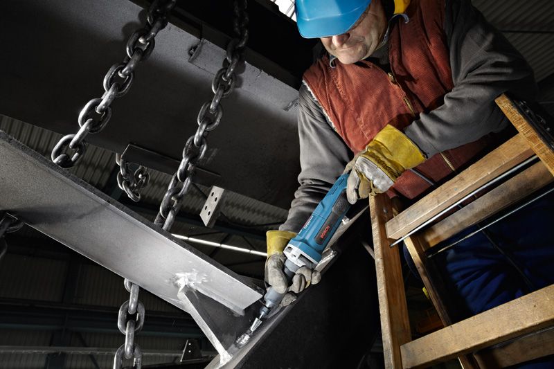 En person som bär säkerhetsutrustning slipar en metallbalk med en rak slipmaskin.