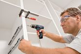 En person som bär säkerhetsutrustning använder en sladdlös borrmaskin för att montera ett skåp.