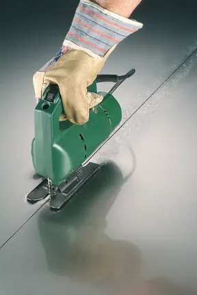 En person som bär säkerhetsutrustning använder en sticksåg för att såga en rak linje i metall.