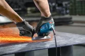 En person med säkerhetsutrustning slipar metall och skapar gnistor med en vinkelslip.