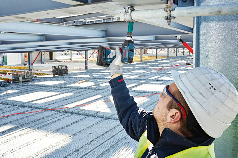 En person som bär säkerhetsutrustning använder en sladdlös slagnyckel på en metallbalk.