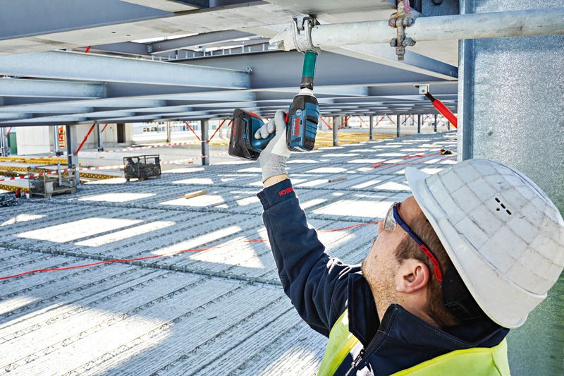 En person som bär säkerhetsutrustning använder en sladdlös slagnyckel på en metallbalk.