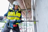 En person med säkerhetsutrustning borrar i betong med en sladdlös borrhammare.