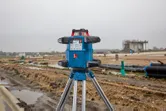 Lasernivelleringsverktyg på ett stativ står på en våt byggarbetsplats.
