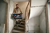 En person med säkerhetsutrustning bär en sladdlös bordsåg nerför en trappa.