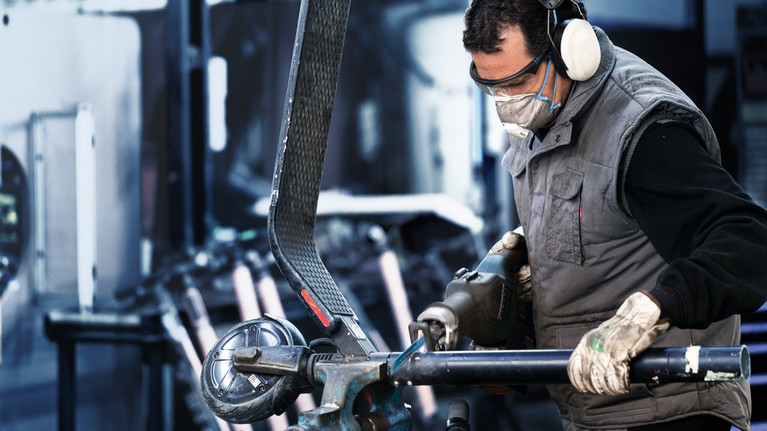 En person med säkerhetsutrustning slipar ett metallrör i en industriell verkstad.