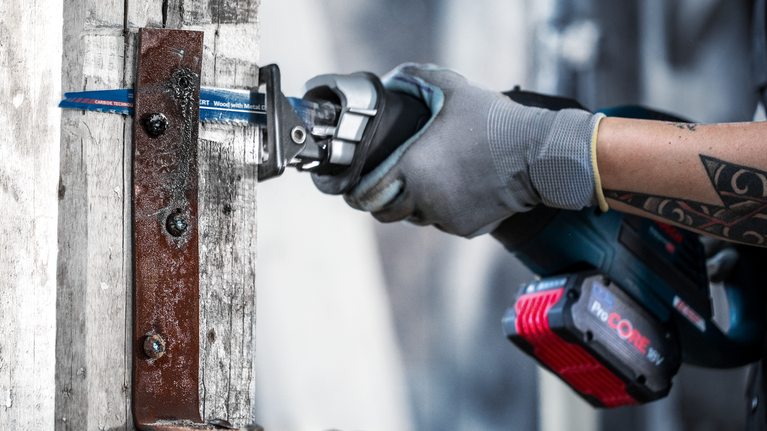 En person som bär säkerhetsutrustning använder en fram- och återgående såg för att såga en metallplåt.