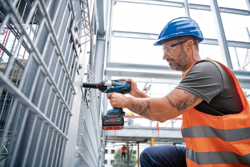 En person som bär säkerhetsutrustning använder en sladdlös slagnyckel för att fästa ett metallstaket.