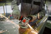En person med säkerhetsutrustning slipar metall med en vinkelslip, vilket producerar gnistor.
