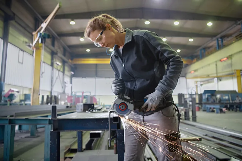 En person med säkerhetsutrustning slipar metall på en arbetsbänk, vilket producerar gnistor.