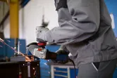 En person med säkerhetsutrustning slipar metall, vilket producerar gnistor i en verkstad.