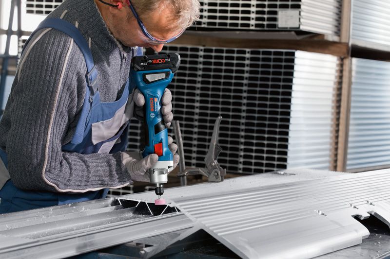 En person med säkerhetsutrustning slipar en metallplåt med en sladdlös rak slipmaskin.