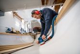 En person med säkerhetsutrustning slipar insidan av ett träbåtsskrov.