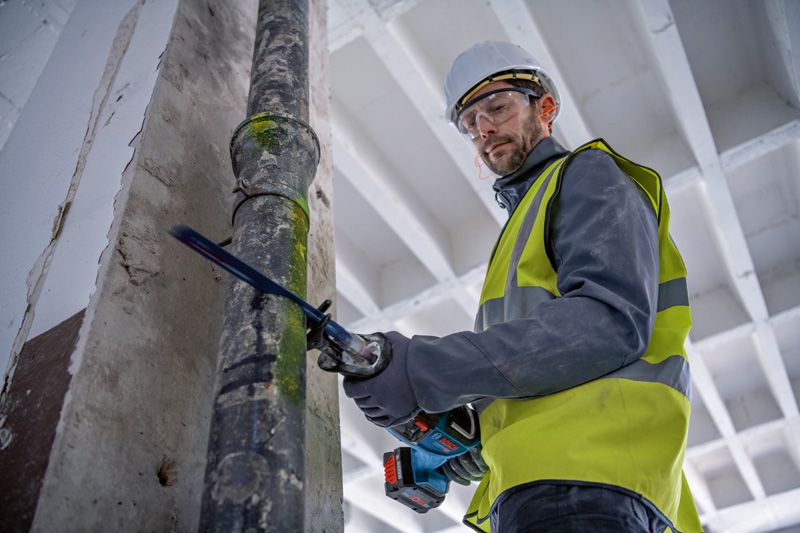 En person som bär säkerhetsutrustning sågar ett metallrör med en fram- och återgående såg.