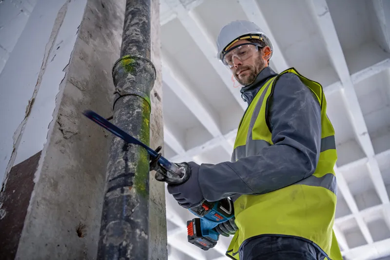 En person som bär säkerhetsutrustning sågar ett metallrör med en fram- och återgående såg.
