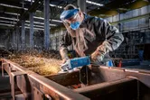 En person med säkerhetsutrustning slipar metall med en vinkelslip, gnistor flyger.