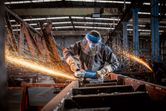 En person med säkerhetsutrustning slipar metall, vilket producerar ljusa gnistor i en fabrik.