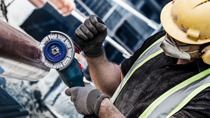 En person som bär säkerhetsutrustning använder en vinkelslip för att skära ett metallrör.