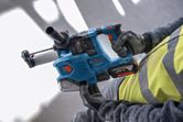 En person med säkerhetsutrustning håller en sladdlös borrhammare.