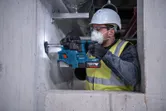 En person med säkerhetsutrustning borrar i en betongvägg med en borrhammare.