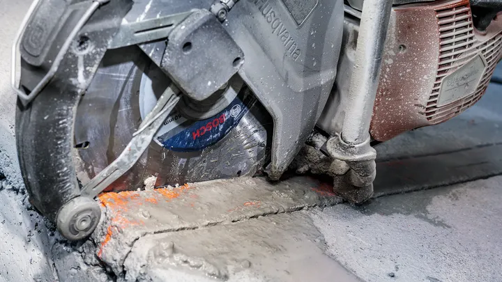 Betongsåg skär igenom en cementyta med synligt damm och slam.